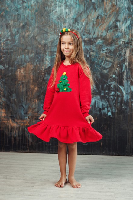 Girl's red dress with a ruffle and a decorated Christmas tree